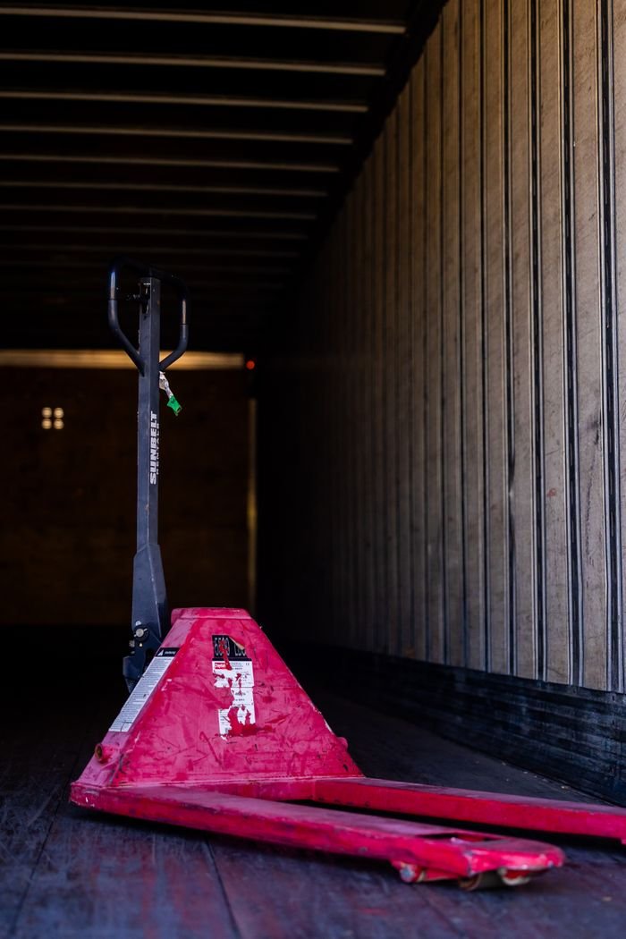 Red pallet jack inside an empty truck trailer, showcasing industrial transport equipment.